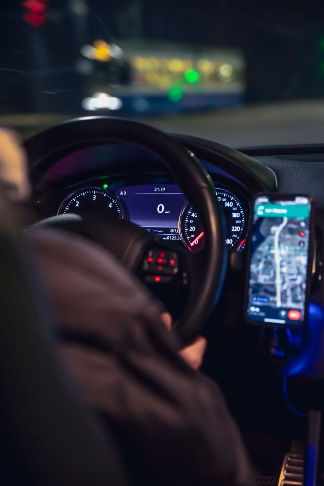 Motorista ao volante à noite, com o celular preso ao suporte do painel.