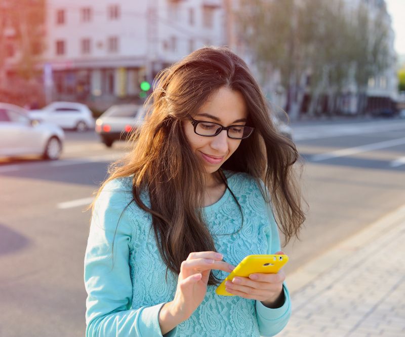 Passageira sorrindo enquanto usa o celular em uma rua com carros ao fundo.